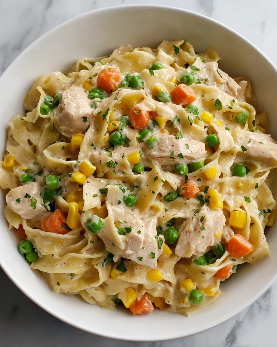 A white bowl filled with creamy pasta showing three layers: the bottom layer of flat, wide noodles in a light cream sauce; the middle layer with chunks of light beige cooked chicken evenly spread; and the top layer with colorful vegetables including bright green peas, orange carrot pieces, and yellow corn kernels mixed throughout. Small green herb bits are sprinkled over the dish, adding texture and color contrast. The bowl sits on a surface with a white marbled texture. Photo taken with an iphone --ar 4:5 --v 7