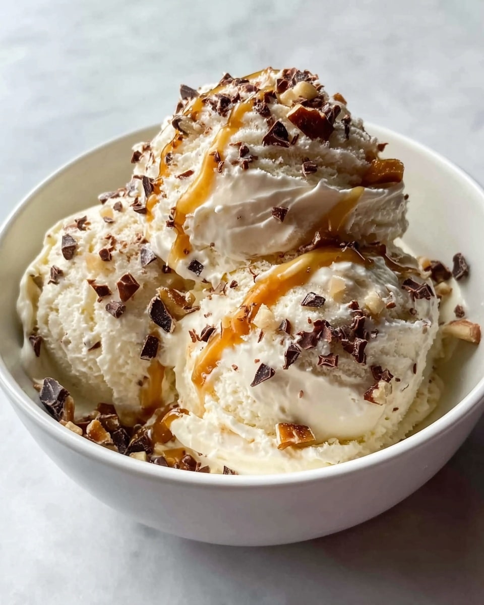 A white bowl filled with several scoops of creamy off-white ice cream, topped with scattered small dark brown chocolate pieces and a few light brown nut fragments, along with drizzles of golden caramel sauce on top. The bowl is placed on a white marbled surface. photo taken with an iphone --ar 4:5 --v 7