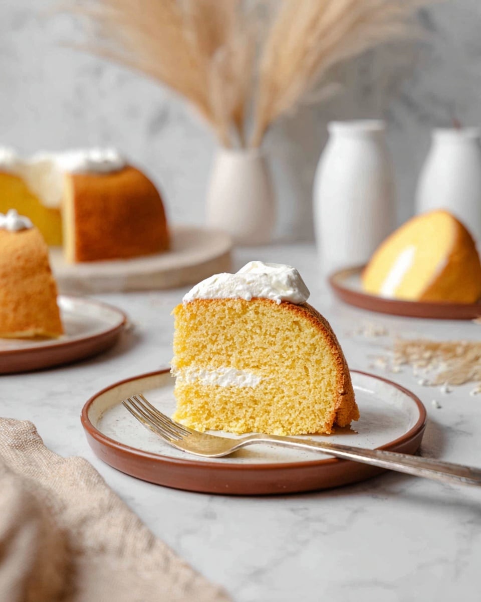 A round bundt cake with a golden brown crust sits on a white plate. The cake has a smooth, slightly shiny texture with gentle ridges running from the center hole to the edges. It is lightly dusted with white powdered sugar, creating a soft contrast on the top and some around the base. The background is a white marbled surface that adds a clean and simple look to the scene. photo taken with an iphone --ar 4:5 --v 7