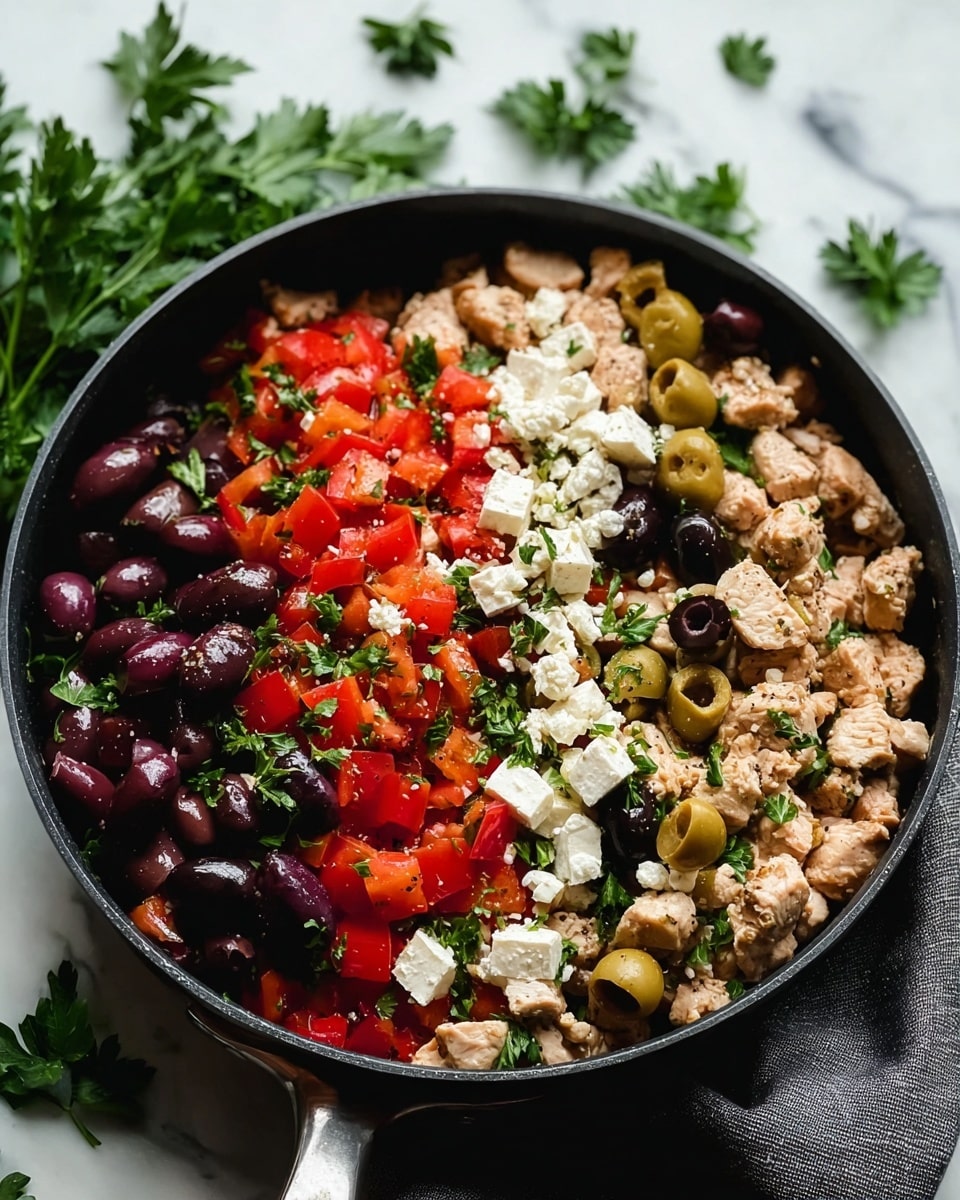 A black pan filled with a colorful Greek salad mix, showing layers of small chunks of cooked chicken, bright red chopped tomatoes, white cubes of feta cheese, plump dark purple olives, and green olive slices, all sprinkled with fresh green parsley leaves. The pan rests on a gray cloth on a white marbled surface, with scattered green parsley leaves around it for decoration. The textures contrast between soft cheese, juicy tomatoes, and meaty chicken. photo taken with an iphone --ar 4:5 --v 7