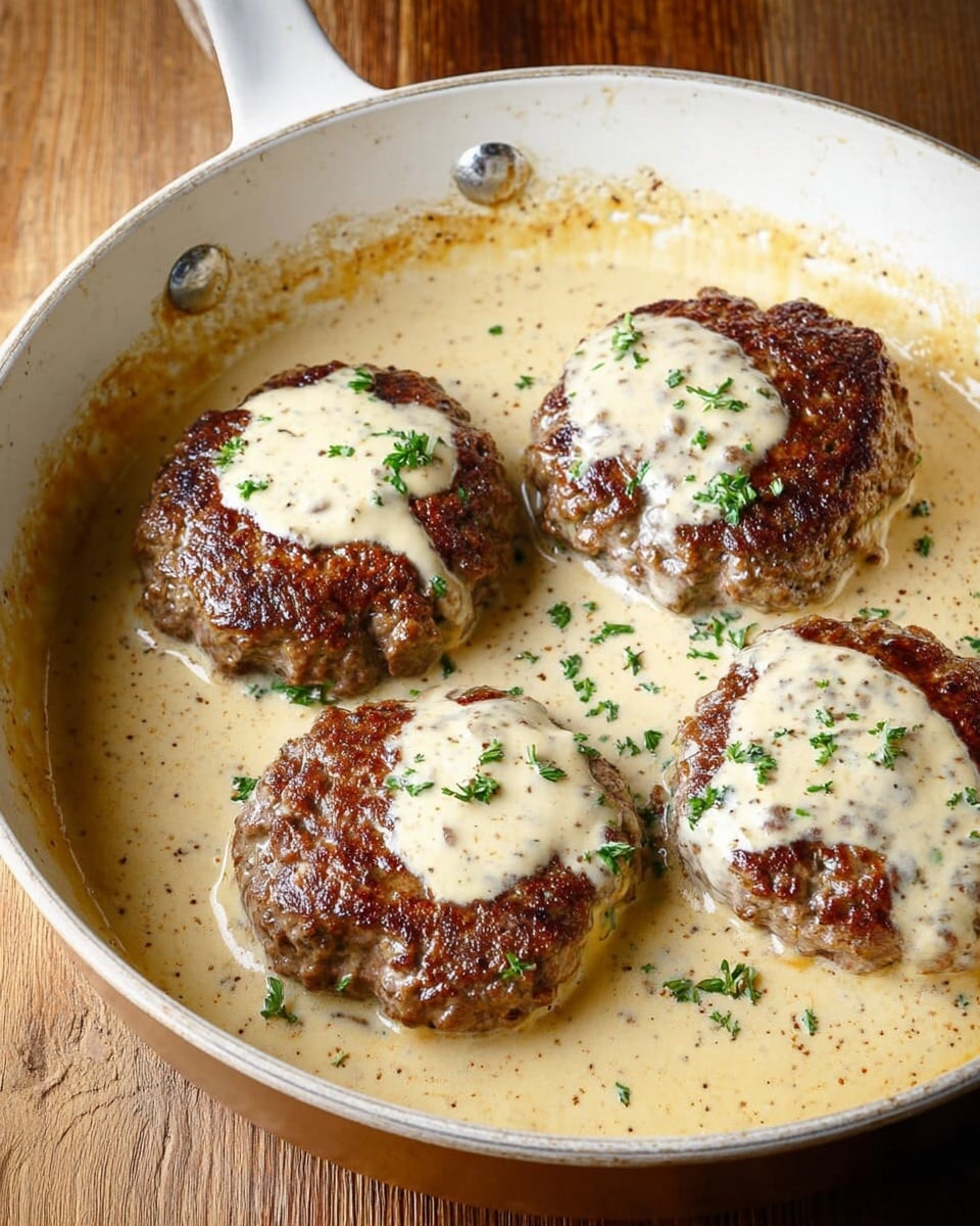 The image shows a white pan filled with four browned meat patties in a creamy beige sauce. Each patty has a dollop of sauce on top, with small green herb bits sprinkled over the meat and sauce. The creamy sauce surrounds the patties, covering the bottom of the pan, and has a smooth, slightly speckled texture. The pan rests on a wooden surface. photo taken with an iphone --ar 4:5 --v 7