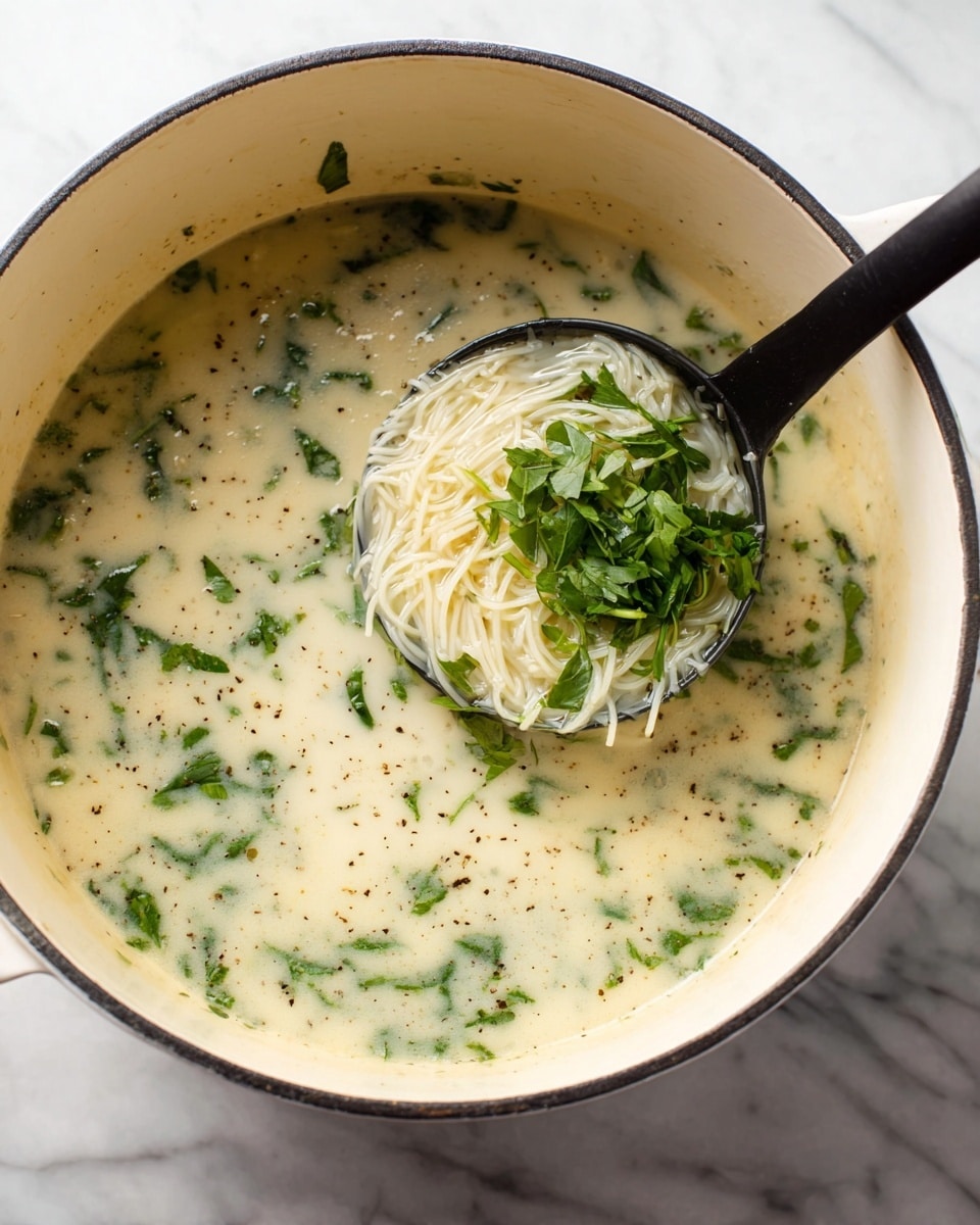 A large white pot filled with creamy white broth soup with visible specks of black pepper and chopped green herbs floating evenly throughout. A black ladle inside the pot holds a bundle of thin, pale white noodles mixed with green leafy herbs, lifted slightly above the broth. The pot is on a white marbled surface, and the soup has a smooth and slightly thick texture with fresh herbs giving a vibrant green contrast. photo taken with an iphone --ar 4:5 --v 7