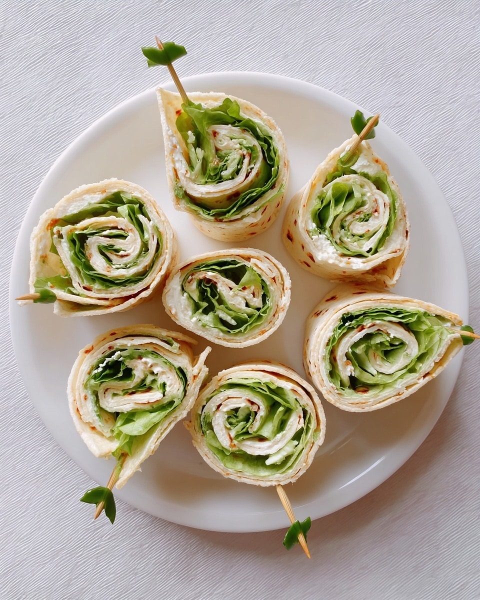 Six pinwheel wraps are neatly arranged on a white plate sitting on a white marbled surface. Each wrap has three visible layers: a light beige flatbread outer layer, a creamy white spread inside, and fresh green lettuce leaves in the middle. The wraps are cut into round spirals, and each is secured with a wooden toothpick with a small green decoration at the end. The simple colors and clean arrangement make the dish look fresh and inviting. Photo taken with an iphone --ar 4:5 --v 7