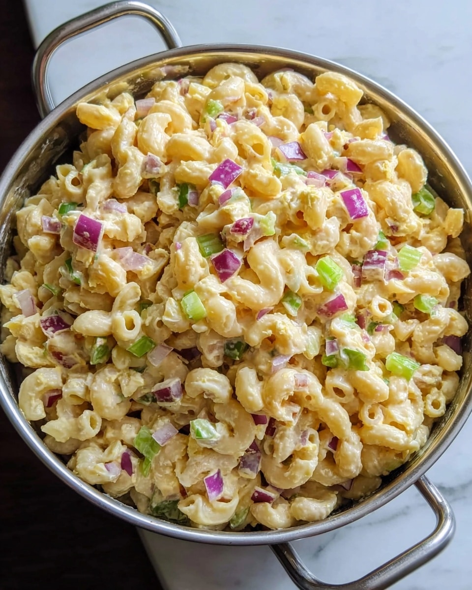 A bowl filled with three layers of food starts with pale creamy macaroni pasta at the bottom, mixed with small pieces of red onion and celery that add purple and green bits throughout. The middle layer is lightly dusted with a bright orange powder, likely paprika, spread evenly over the pasta. The top layer shows fresh chopped green chives sprinkled generously, giving a sharp contrast with the creamy and orange tones underneath. The bowl is round with silver handles on each side, sitting on a dark surface that is replaced by a white marbled texture. photo taken with an iphone --ar 4:5 --v 7