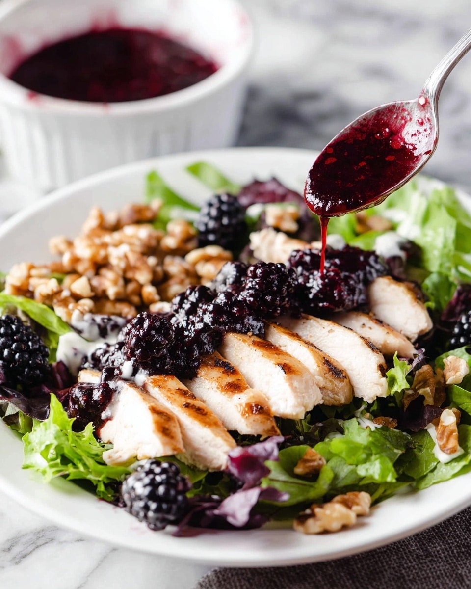 A white plate holds a fresh salad with layered ingredients: at the bottom is a bed of mixed green and purple leafy lettuce, topped with sliced grilled chicken breast arranged in a neat row, its color light with grill marks. On top of the chicken are dollops of a dark, glossy blackberry sauce with visible whole blackberries scattered on the salad. To one side of the plate are chopped walnuts, adding texture and a light brown color contrast. A spoon is seen pouring more of the deep red-purple blackberry sauce over the chicken. In the background, a white bowl filled with more of the dark berry sauce sits on a white marbled surface. photo taken with an iphone --ar 4:5 --v 7