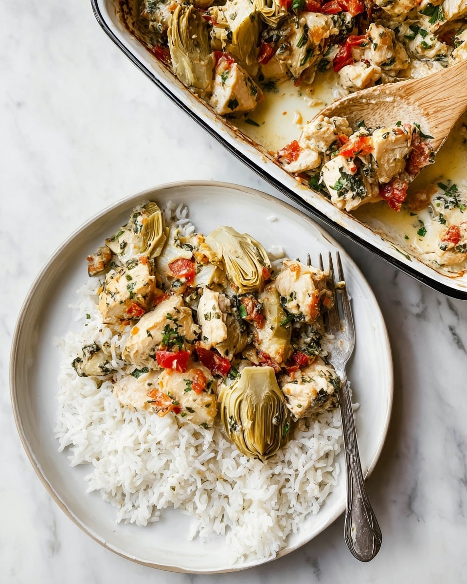 A white round plate with two main layers is shown on a white marbled surface. On the right side of the plate, there is a layer of fluffy white rice with separate grains, while on the left side, chunks of creamy, herb-covered chicken mixed with red pepper pieces and large, soft, pale yellow artichoke hearts sit on the rice layer, showing a mix of green herbs and diced vegetables on the chicken. A silver fork rests on the right edge of the plate near the rice. In the top right corner of the image, a white enamel baking dish with black trim filled with the same chicken and artichoke mix is visible, with a wooden spoon scooping the dish. Photo taken with an iphone --ar 4:5 --v 7