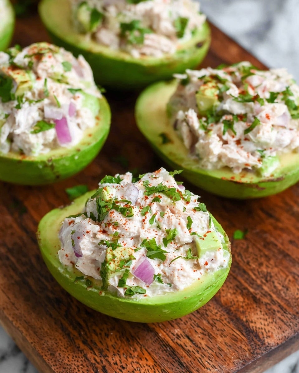 The image shows green avocado halves each filled with a creamy chicken salad that has small pieces of red onion and is topped with chopped green herbs and a sprinkle of red seasoning. The smooth green avocado acts as the base layer, while the white and light pink chicken salad forms the thick middle layer, garnished with bright green herbs and red seasoning on top. The avocados are placed closely together on a brown wooden board. The background texture is changed to white marble. photo taken with an iphone --ar 4:5 --v 7