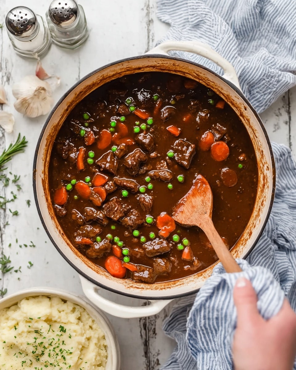 A white round pot filled with a thick dark brown stew that has visible chunks of beef, bright orange carrots, and small green peas, stirred by a wooden spoon held by a woman's hand wearing a blue and white striped cloth; the stew has a glossy, rich texture with bits of sauce coating the pot’s sides. A bowl of creamy mashed potatoes garnished with herbs is partly visible in the bottom left corner, placed on a white marbled texture surface, alongside a glass bottle and two metal shakers near the top left. A bulb of garlic and a sprig of green rosemary rest near the pot’s handle on the white marbled background photo taken with an iphone --ar 4:5 --v 7