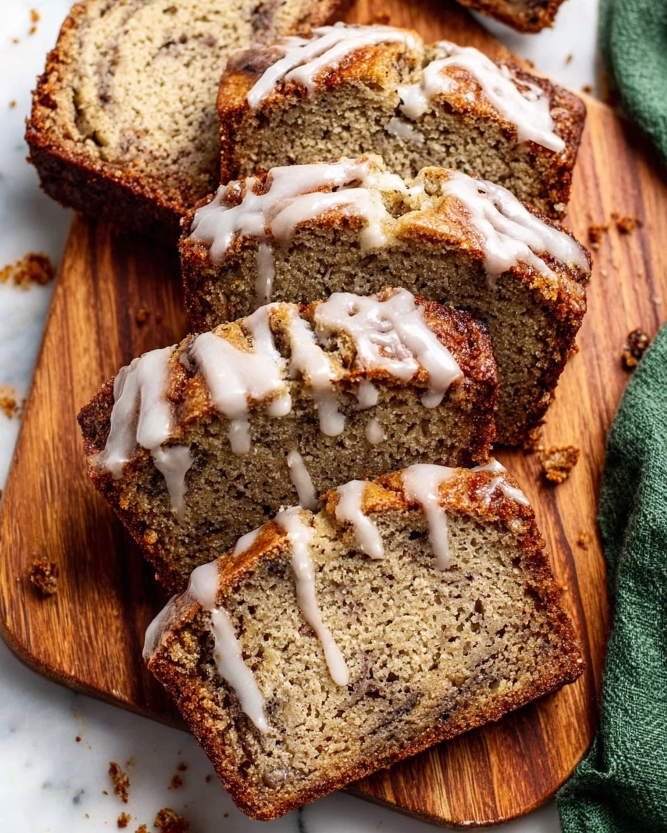 The image shows several thick slices of moist banana bread arranged on a wooden cutting board. Each slice has a speckled light brown color with darker spots from mashed bananas and bits of nuts or spices inside. Thin white lines of icing drizzle irregularly across the top of the slices, adding a creamy texture that contrasts with the denser bread below. Crumbs from the bread are scattered near the edges, suggesting a soft and crumbly texture. The background is a white marbled surface with a folded green cloth partially visible on the right side. Photo taken with an iphone --ar 4:5 --v 7