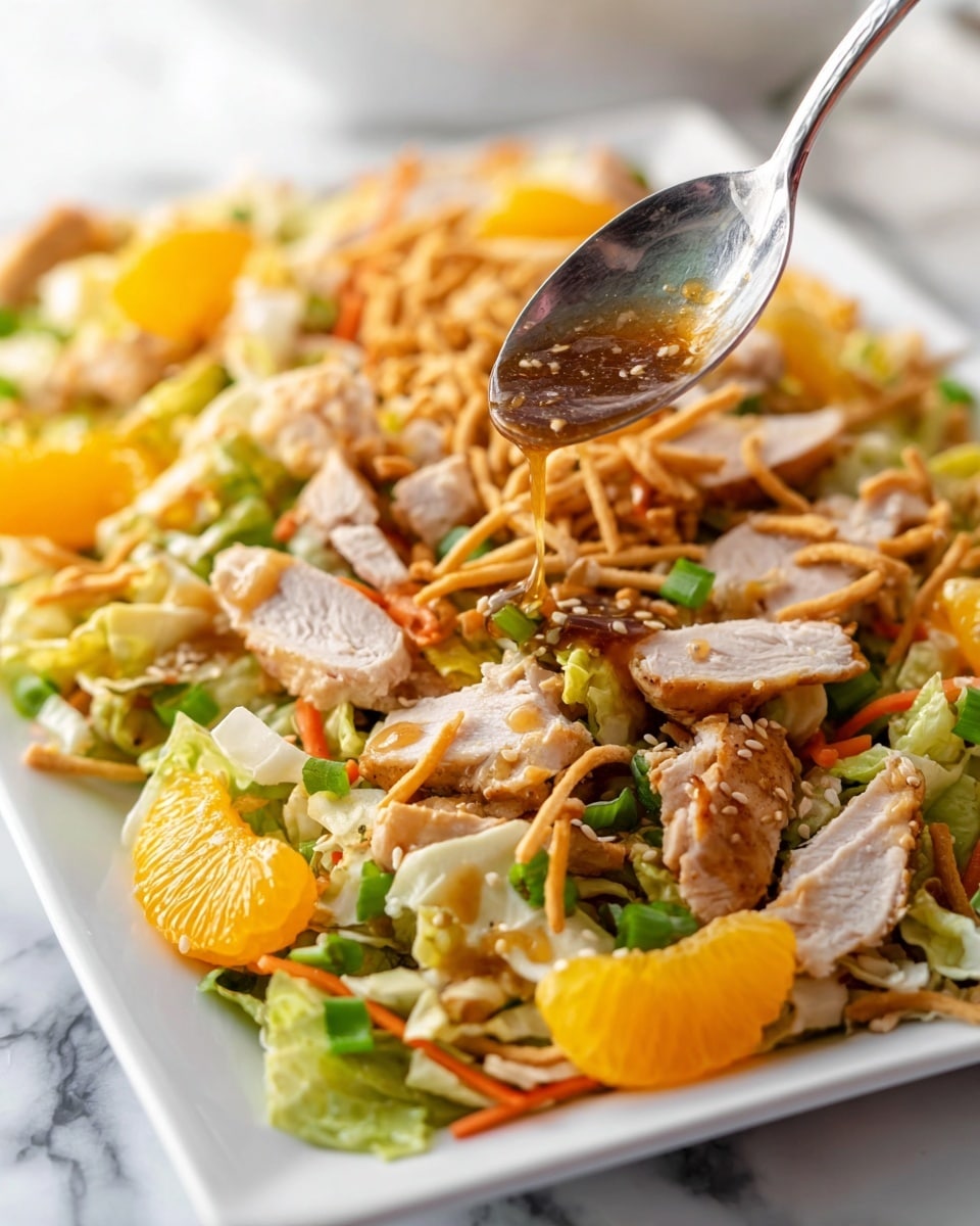 A white octagonal plate holds a colorful layered salad. The base layer is light green chopped lettuce with thin orange carrot sticks mixed in. On top are medium-sized chunks of grilled chicken, scattered bright orange mandarin slices, and thinly sliced green onions. Crunchy golden fried wonton strips and curly crispy noodles add texture, sprinkled with pale almond slices and small white sesame seeds. The salad is lightly drizzled with a glossy brown dressing. A large silver spoon rests on the right side of the plate. The plate is on a white marbled surface, with a soft white cloth in the background. photo taken with an iphone --ar 4:5 --v 7
