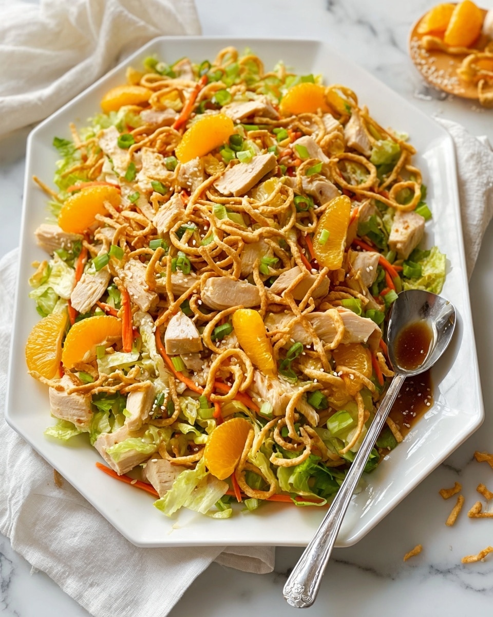 A white rectangular plate holds a colorful layered salad. The base layer is a mix of light green lettuce and shredded cabbage. Scattered on top are bright orange mandarin slices and thin orange carrot strips. Chunks of cooked chicken with a browned outside are spread evenly throughout. Thin, light brown crunchy noodle strips and sprinkled sesame seeds add texture over the salad. Bright green chopped scallions are scattered on top. A silver spoon holds brown dressing just above the salad, with some dressing drizzling onto the chicken and mandarin slices. The surface beneath is a white marbled texture. Photo taken with an iphone --ar 4:5 --v 7