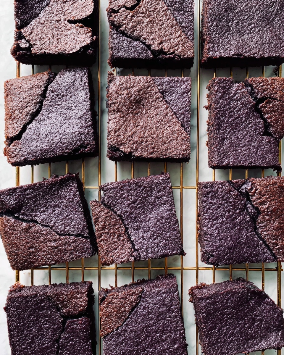 The image shows a cooling rack with multiple square pieces of dark purple brownies laid out in a neat arrangement. Each brownie has a cracked top with a slightly rough texture, showing dense and moist interiors. The edges are a bit sharper, while the center pieces have soft, uneven cracks. The brownies are uniform in size, and the overall look gives a rich, fudgy feel. The background is a white marbled surface. Photo taken with an iphone --ar 4:5 --v 7