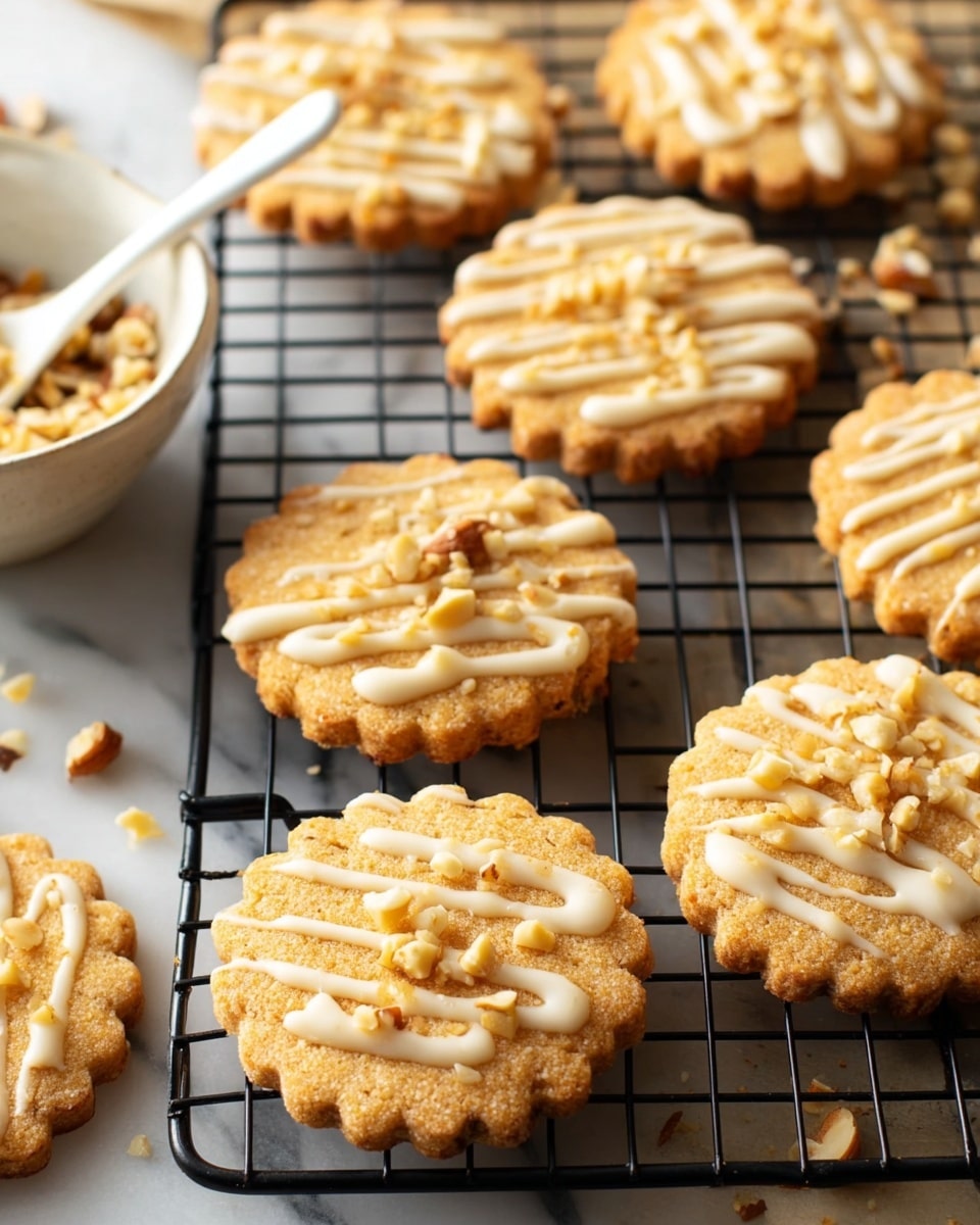 Several round, scalloped-edge cookies with a light golden-brown color sit on a black cooling rack. Each cookie is topped with a pale cream-colored drizzle in thin, uneven lines and small pieces of chopped nuts scattered on top. The cooling rack is placed on a white marbled surface. A white bowl partially filled with more chopped nuts is visible in the left background, along with a white spoon hovering above the rack. Photo taken with an iphone --ar 4:5 --v 7